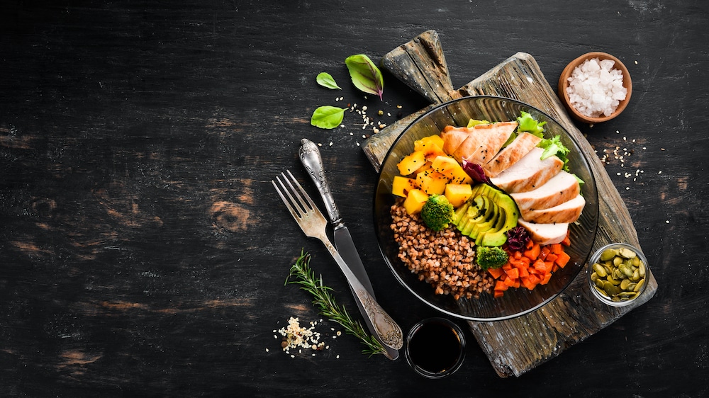 A bowl of chicken salad with vegetables and herbs on a dark wooden table.