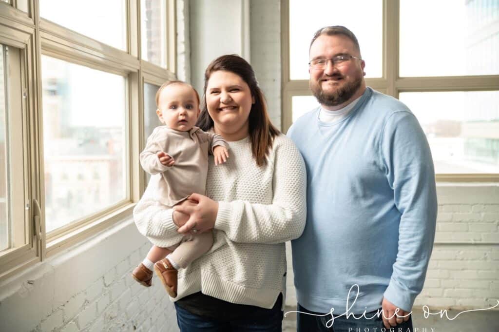 A couple holding a baby in front of a window, celebrating their successful journey through IVF and family planning.
