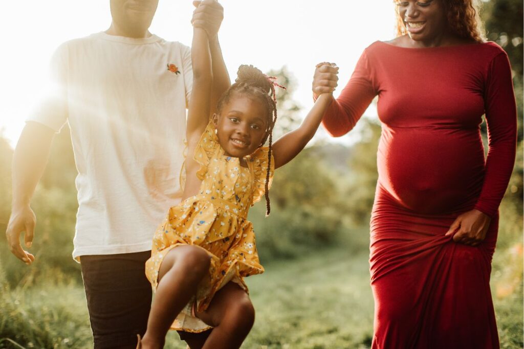 A mother and father playing in a field and holding hands with their daughter. 