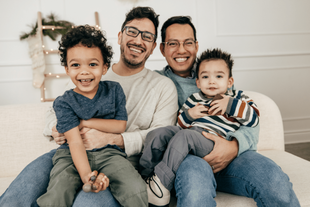 Two men with their two sons smiling for a photograph on a couch