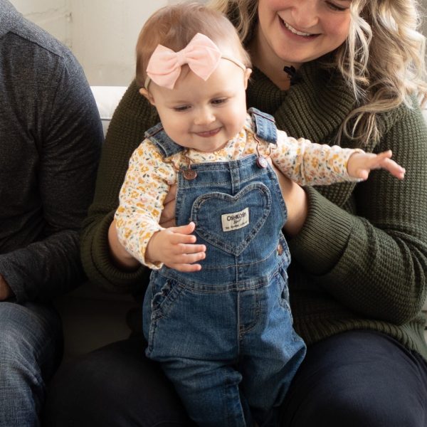 A family sitting on a couch with a baby in overalls, showcasing the joy of family planning.