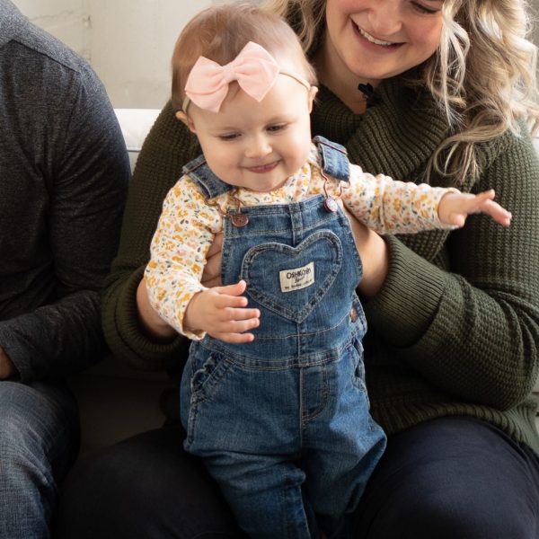 A family sitting on a couch with a baby in overalls, showcasing the joy of family planning.