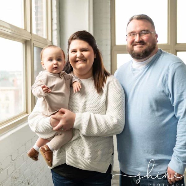 A couple holding a baby in front of a window, celebrating their successful journey through IVF and family planning.