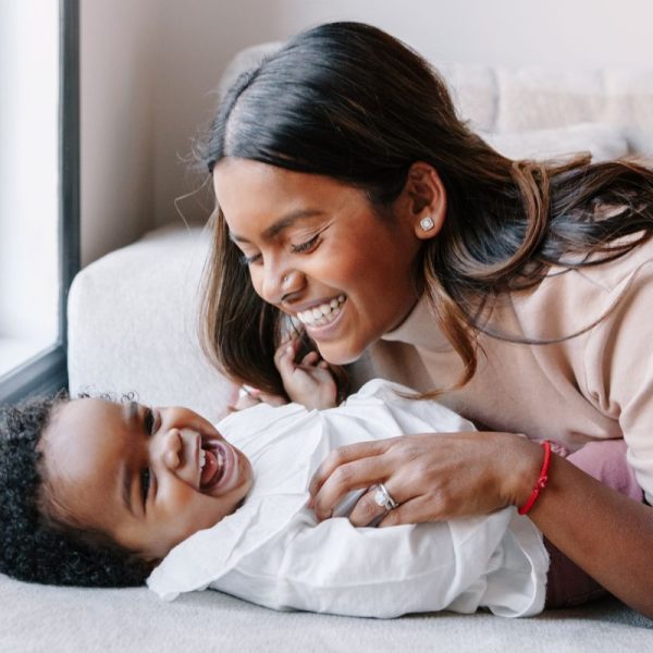 A woman smiles while holding her baby on a couch, cherishing their special bond.