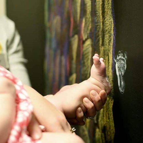 A woman holding a baby's foot in front of a chalkboard, symbolizing the success of her fertility treatment journey with in vitro fertilization.