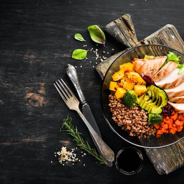 A bowl of chicken salad with vegetables and herbs on a dark wooden table.
