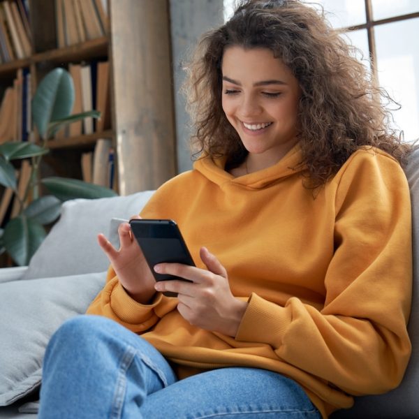 A young woman is sitting on a couch and using her phone to research fertility treatment options.