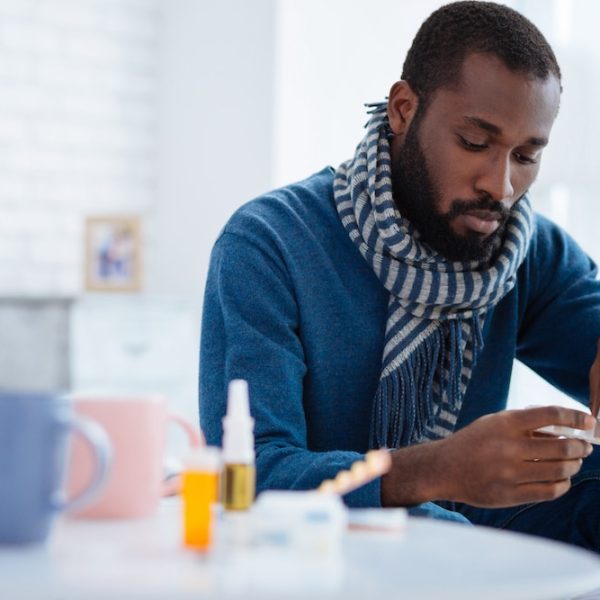 A man is sitting on a bed with a fertility pill in his hand.
